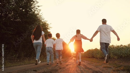 Careful parents with little children run joining hands along road in sunset park