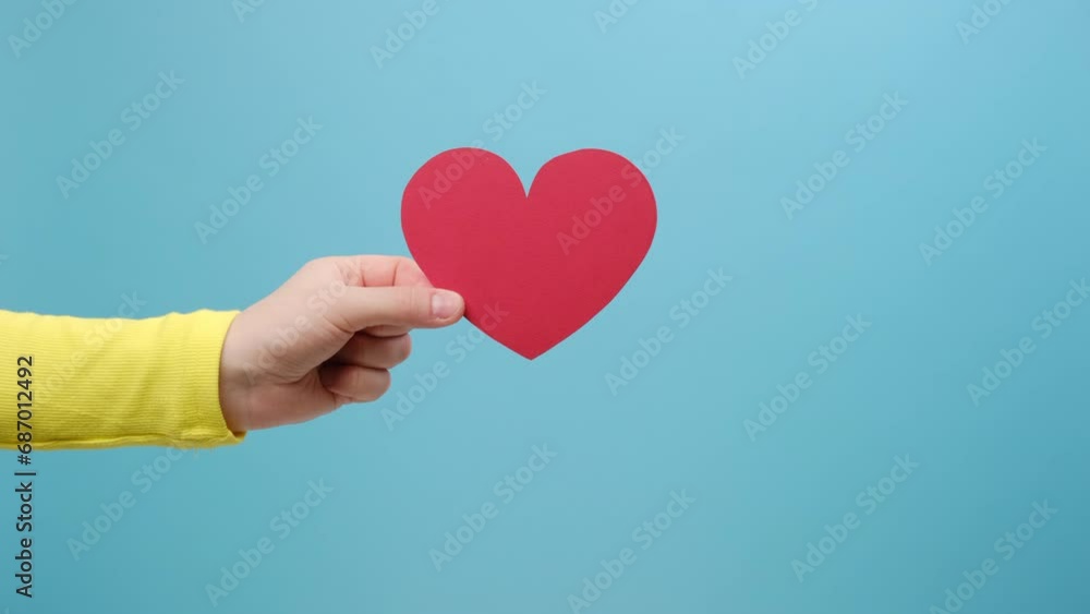 Closeup of female hand holding red heart, cute symbol of sensual feminine romantic love, greeting card on Valentine's day, 14 February concept, isolated over blue color background wall in studio Closeup of female hand holding red heart, cute symbol of sensual feminine romantic love, greeting card on Valentine's day, 14 February concept, isolated over blue color background wall in studio