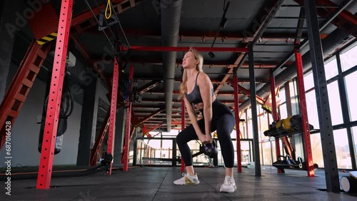 woman trains the muscles of shoulders with kettlebell in gym