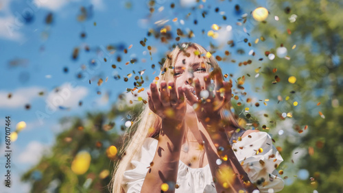 The girl blows a golden confetti out of her hands.