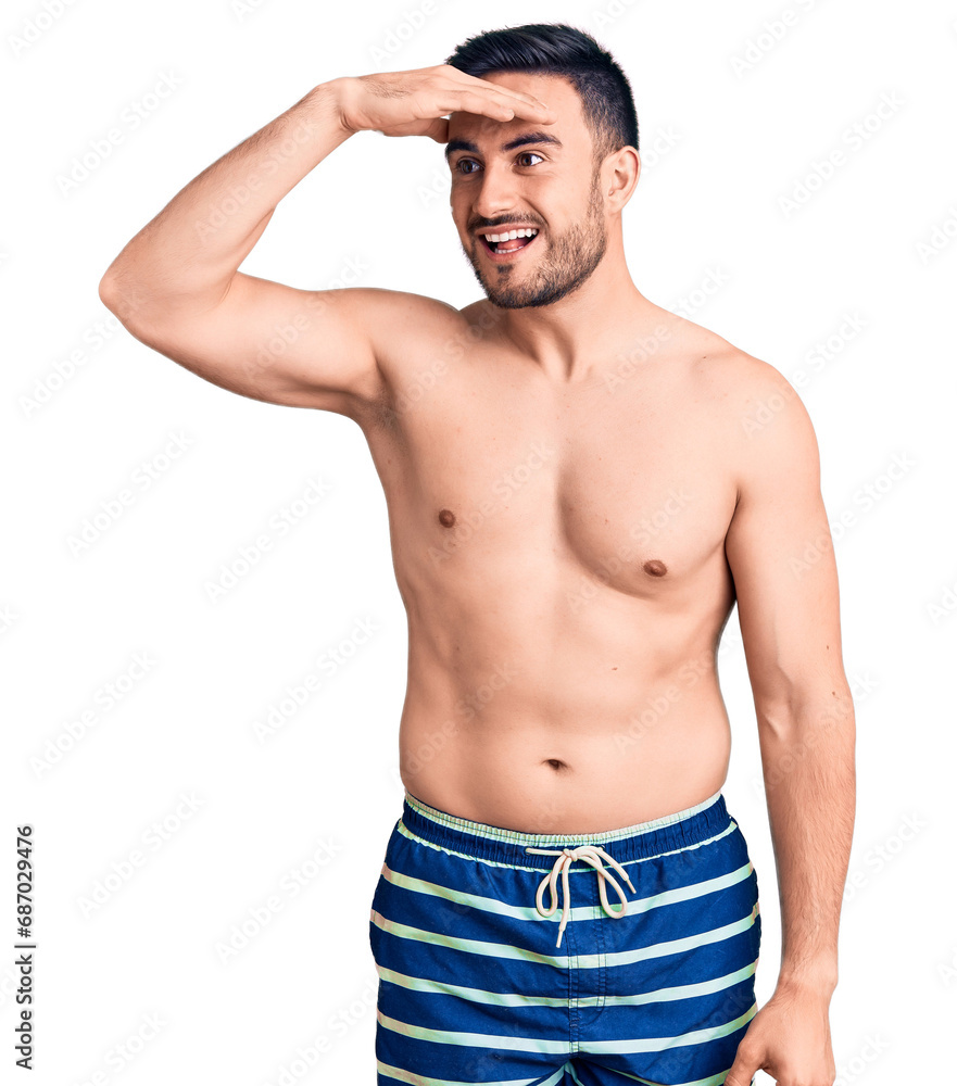 Young handsome man wearing swimwear very happy and smiling looking far away with hand over head. searching concept. Young handsome man wearing swimwear very happy and smiling looking far away with hand over head. searching concept.
