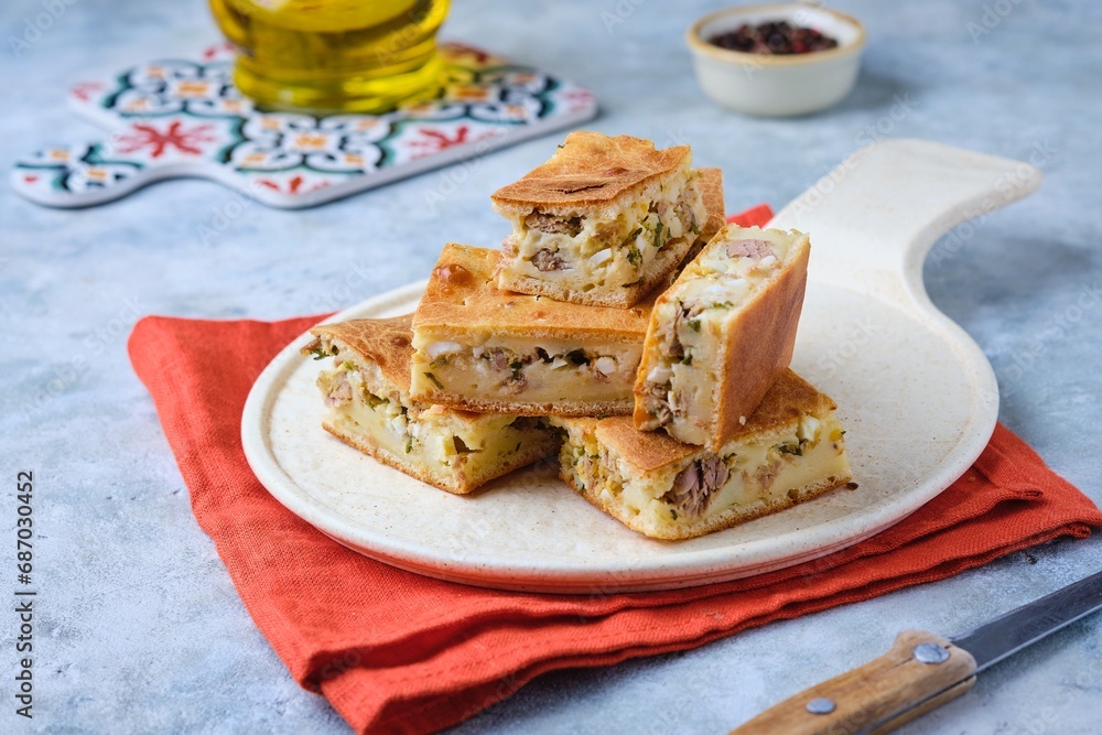 Sliced savory pie with canned tuna, boiled egg and green onions on a ceramic plate on a gray concrete background. Sliced savory pie with canned tuna, boiled egg and green onions on a ceramic plate on a gray concrete background.
