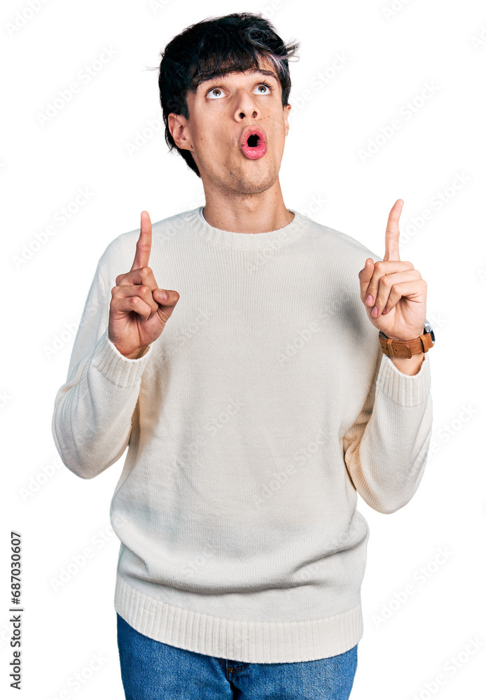 Handsome hipster young man wearing casual winter sweater amazed and surprised looking up and pointing with fingers and raised arms. Handsome hipster young man wearing casual winter sweater amazed and surprised looking up and pointing with fingers and raised arms.