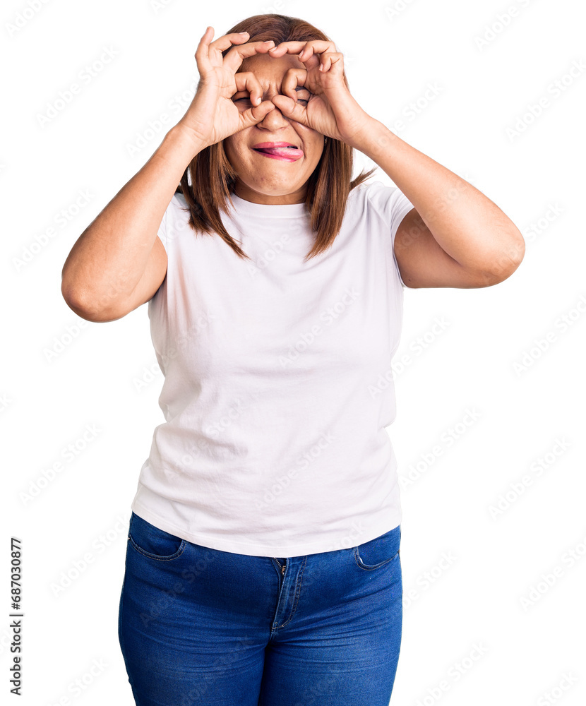 Middle age latin woman wearing casual white tshirt doing ok gesture like binoculars sticking tongue out, eyes looking through fingers. crazy expression. Middle age latin woman wearing casual white tshirt doing ok gesture like binoculars sticking tongue out, eyes looking through fingers. crazy expression.