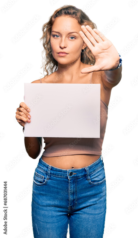 Beautiful caucasian woman holding blank empty banner with open hand doing stop sign with serious and confident expression, defense gesture Beautiful caucasian woman holding blank empty banner with open hand doing stop sign with serious and confident expression, defense gesture