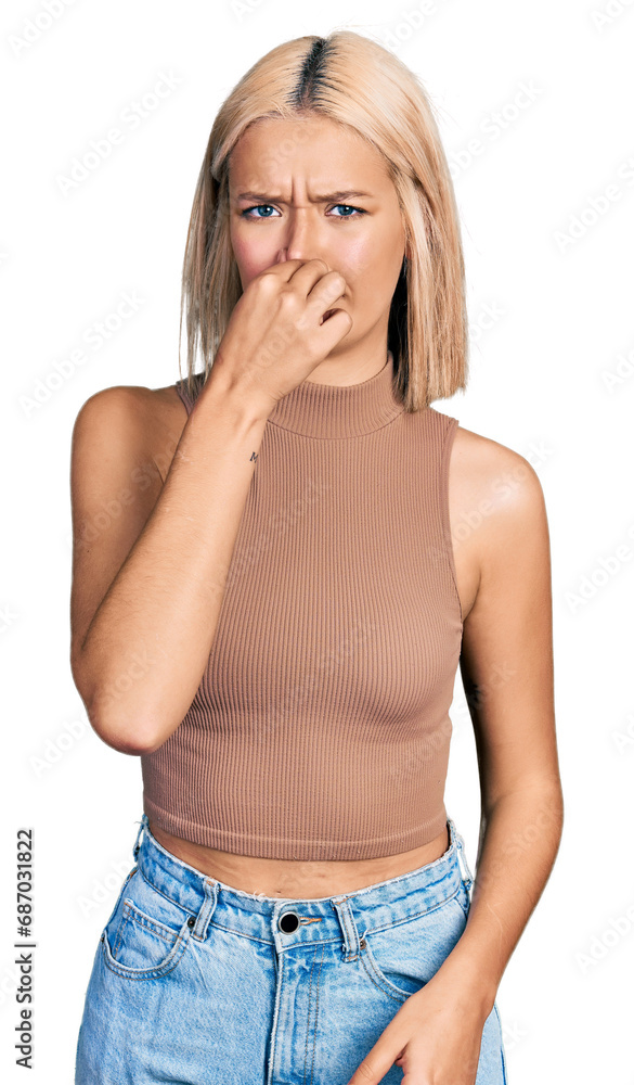 Beautiful young blonde woman wearing casual style with sleeveless shirt smelling something stinky and disgusting, intolerable smell, holding breath with fingers on nose. bad smell Beautiful young blonde woman wearing casual style with sleeveless shirt smelling something stinky and disgusting, intolerable smell, holding breath with fingers on nose. bad smell