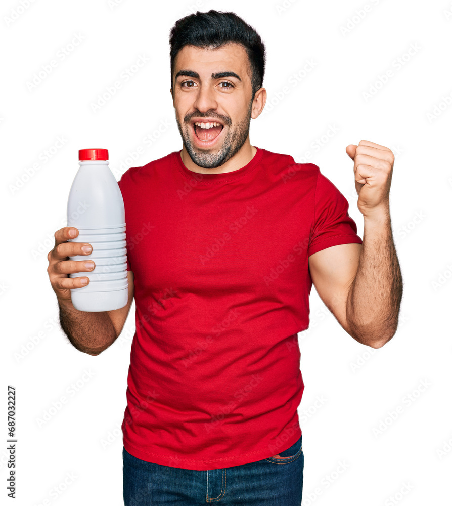 Hispanic man with beard holding liter bottle of milk screaming proud, celebrating victory and success very excited with raised arms Hispanic man with beard holding liter bottle of milk screaming proud, celebrating victory and success very excited with raised arms