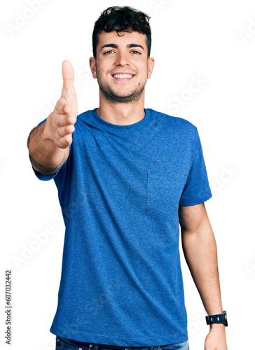 Young hispanic man wearing casual t shirt smiling friendly offering handshake as greeting and welcoming. successful business.