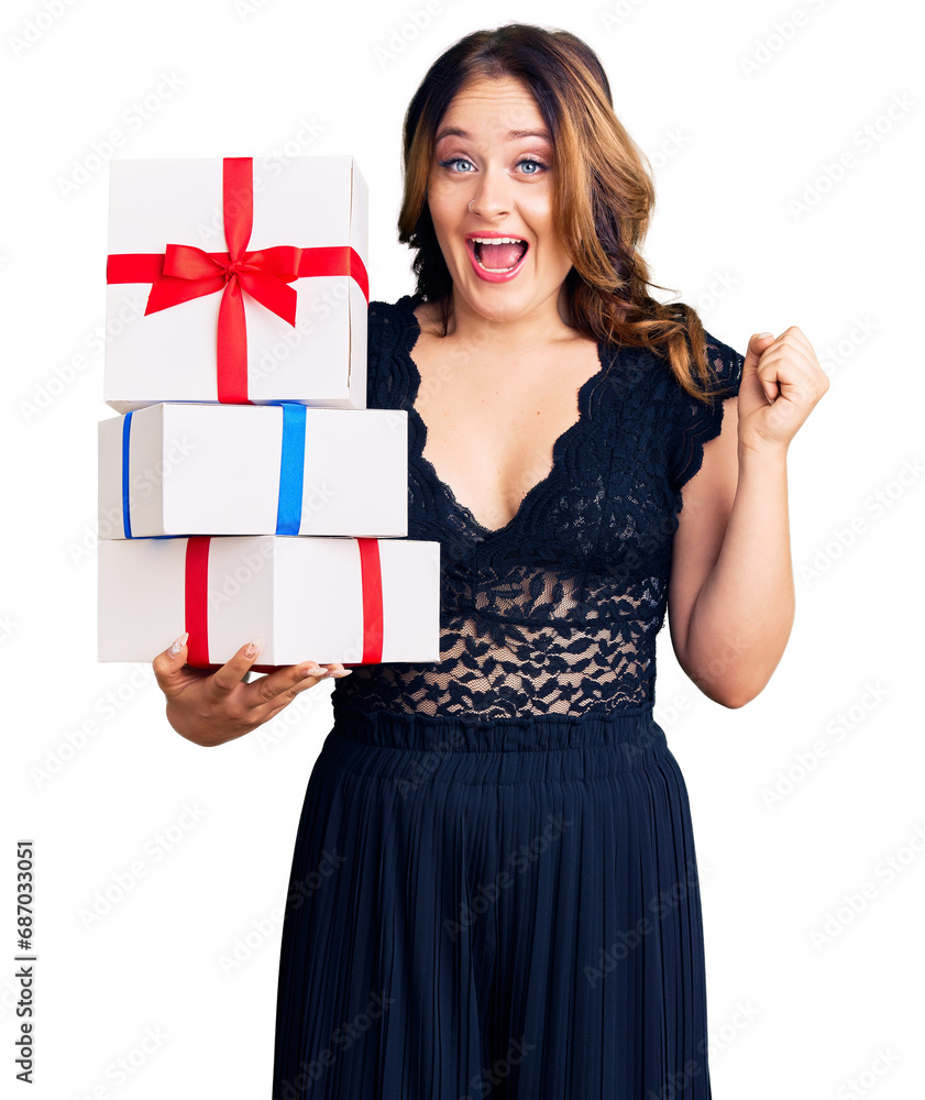 Young beautiful caucasian woman holding gifts screaming proud, celebrating victory and success very excited with raised arms Young beautiful caucasian woman holding gifts screaming proud, celebrating victory and success very excited with raised arms