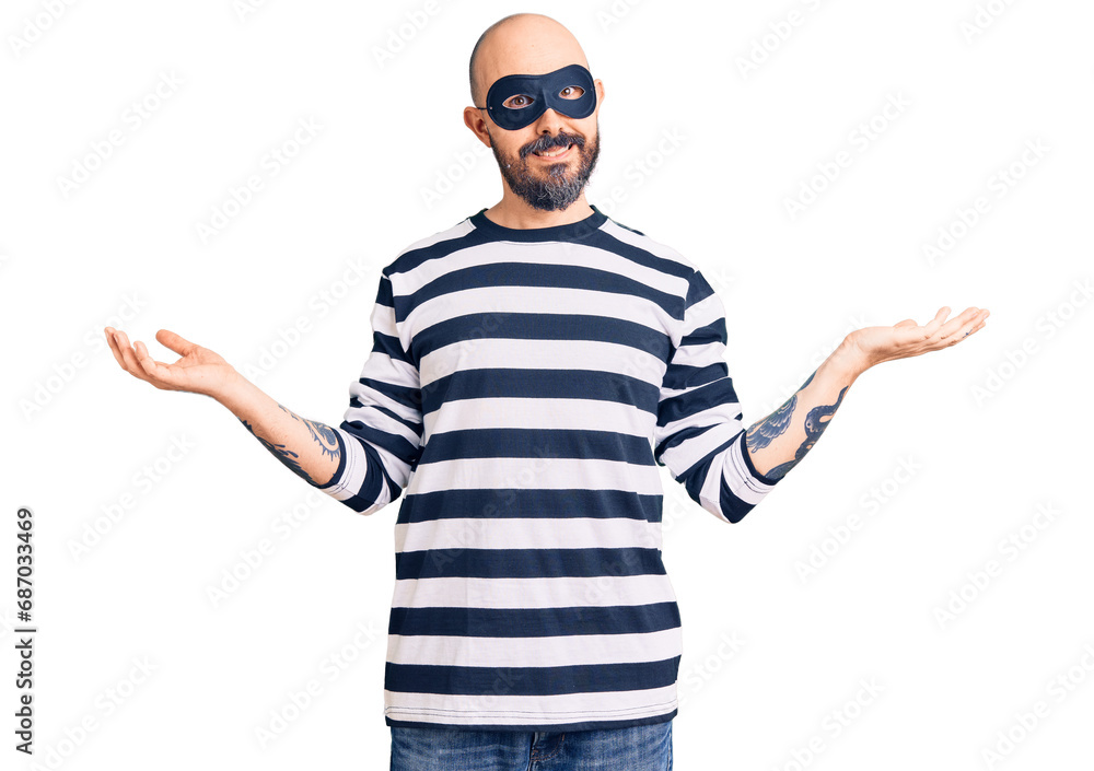 Young handsome man wearing burglar mask smiling showing both hands open palms, presenting and advertising comparison and balance Young handsome man wearing burglar mask smiling showing both hands open palms, presenting and advertising comparison and balance