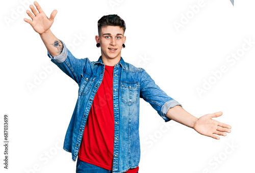 Young caucasian boy with ears dilation wearing casual denim jacket looking at the camera smiling with open arms for hug. cheerful expression embracing happiness.