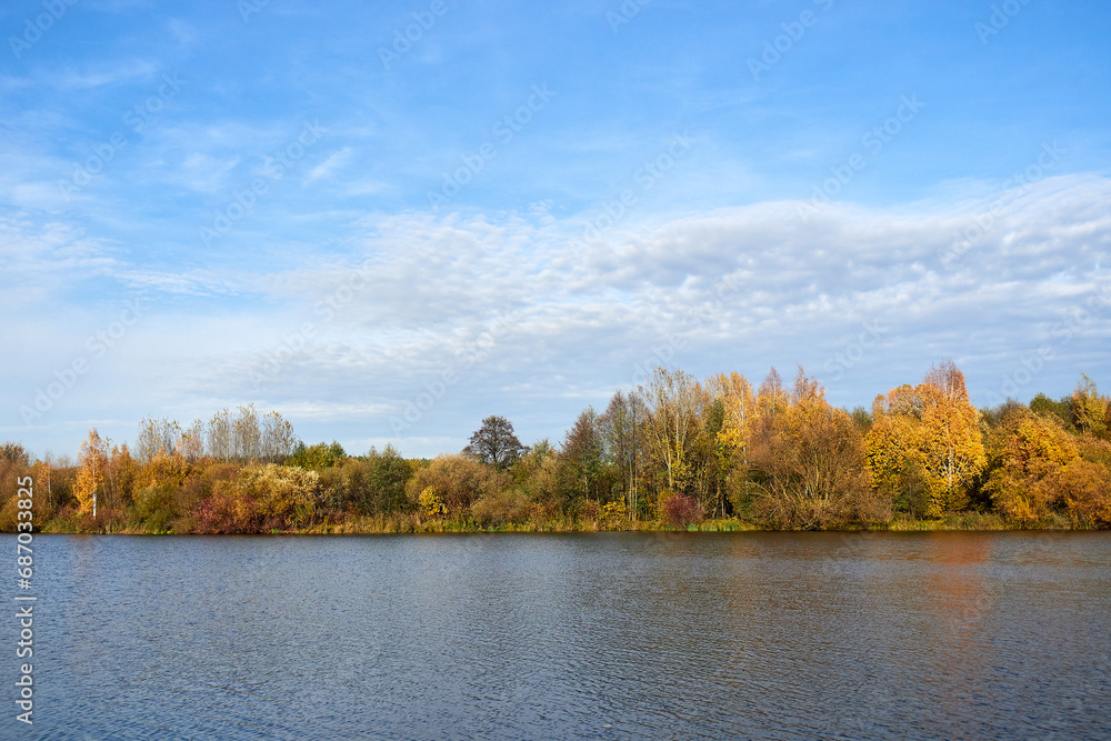 Autumn sunny landscape. Yellow trees and blue sky reflected in the lake