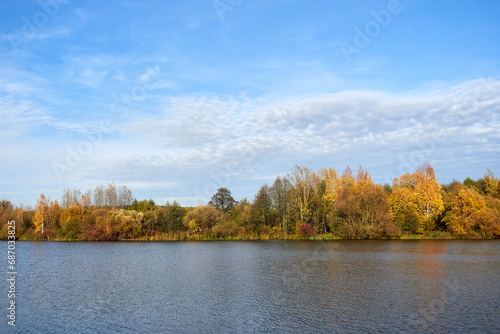 Autumn sunny landscape. Yellow trees and blue sky reflected in the lake