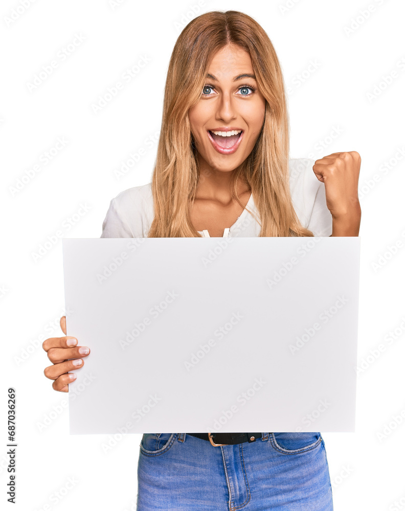 Fototapeta premium Beautiful blonde young woman holding blank empty banner screaming proud, celebrating victory and success very excited with raised arms