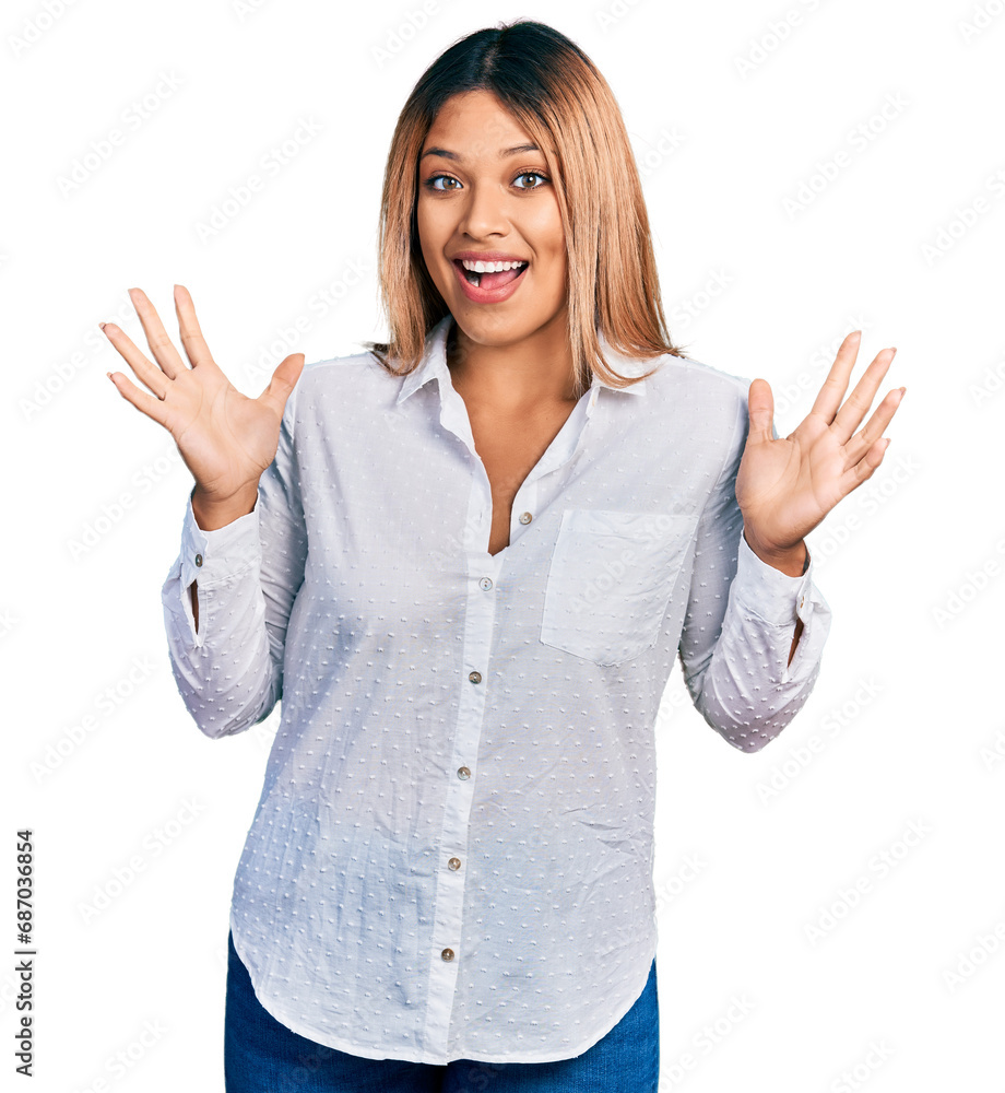 Young hispanic woman wearing casual white shirt celebrating crazy and amazed for success with arms raised and open eyes screaming excited. winner concept Young hispanic woman wearing casual white shirt celebrating crazy and amazed for success with arms raised and open eyes screaming excited. winner concept