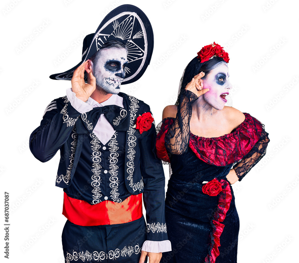 Young couple wearing mexican day of the dead costume over background smiling with hand over ear listening an hearing to rumor or gossip. deafness concept.