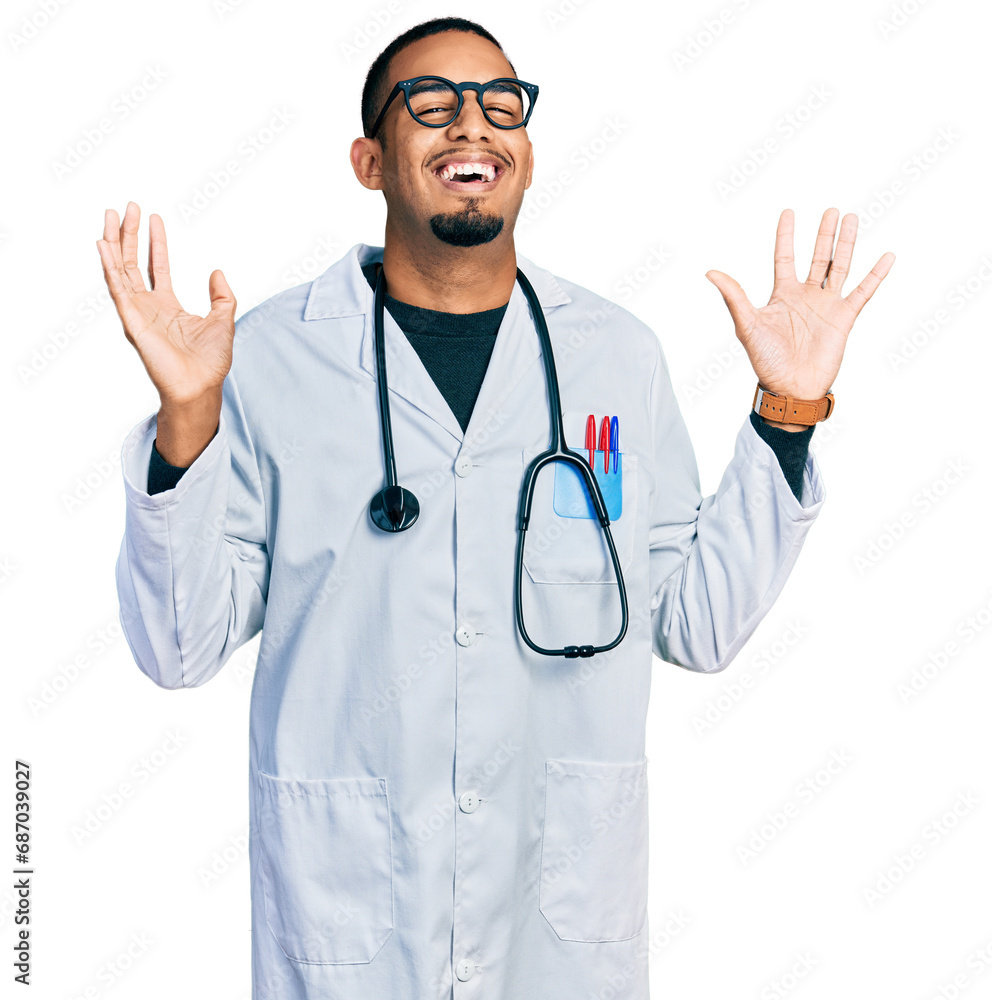 Young african american man wearing doctor uniform and stethoscope celebrating crazy and amazed for success with arms raised and open eyes screaming excited. winner concept Young african american man wearing doctor uniform and stethoscope celebrating crazy and amazed for success with arms raised and open eyes screaming excited. winner concept
