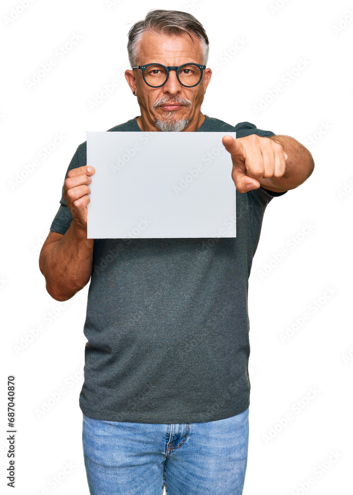 Middle age grey-haired man holding blank empty banner pointing with finger to the camera and to you, confident gesture looking serious Middle age grey-haired man holding blank empty banner pointing with finger to the camera and to you, confident gesture looking serious