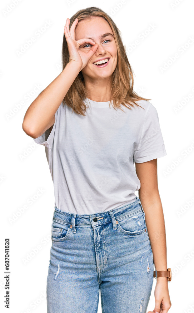 Beautiful young blonde woman wearing casual white t shirt doing ok gesture with hand smiling, eye looking through fingers with happy face. Beautiful young blonde woman wearing casual white t shirt doing ok gesture with hand smiling, eye looking through fingers with happy face.