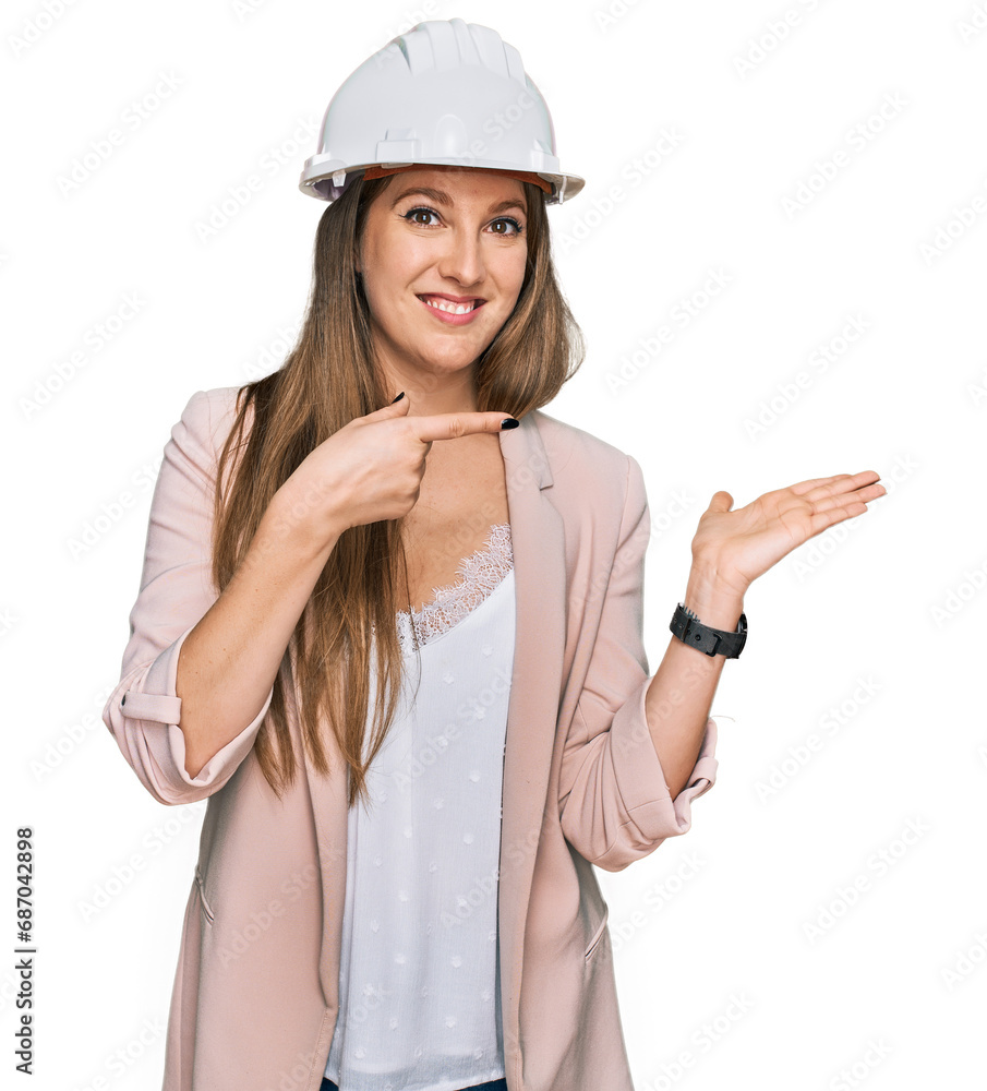 Young blonde woman wearing architect hardhat amazed and smiling to the camera while presenting with hand and pointing with finger. Young blonde woman wearing architect hardhat amazed and smiling to the camera while presenting with hand and pointing with finger.
