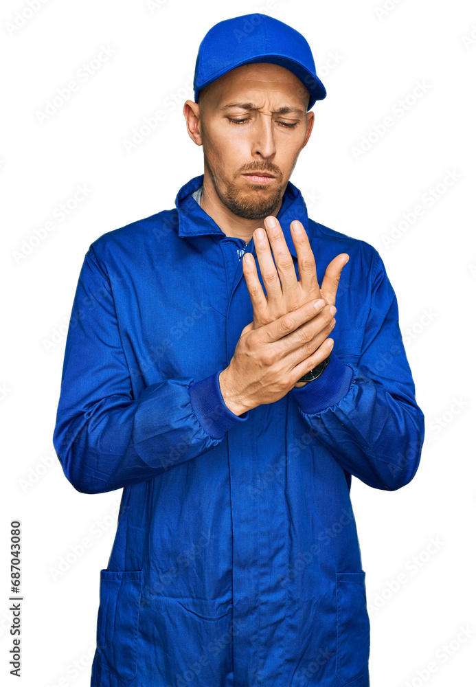 Bald man with beard wearing builder jumpsuit uniform suffering pain on hands and fingers, arthritis inflammation