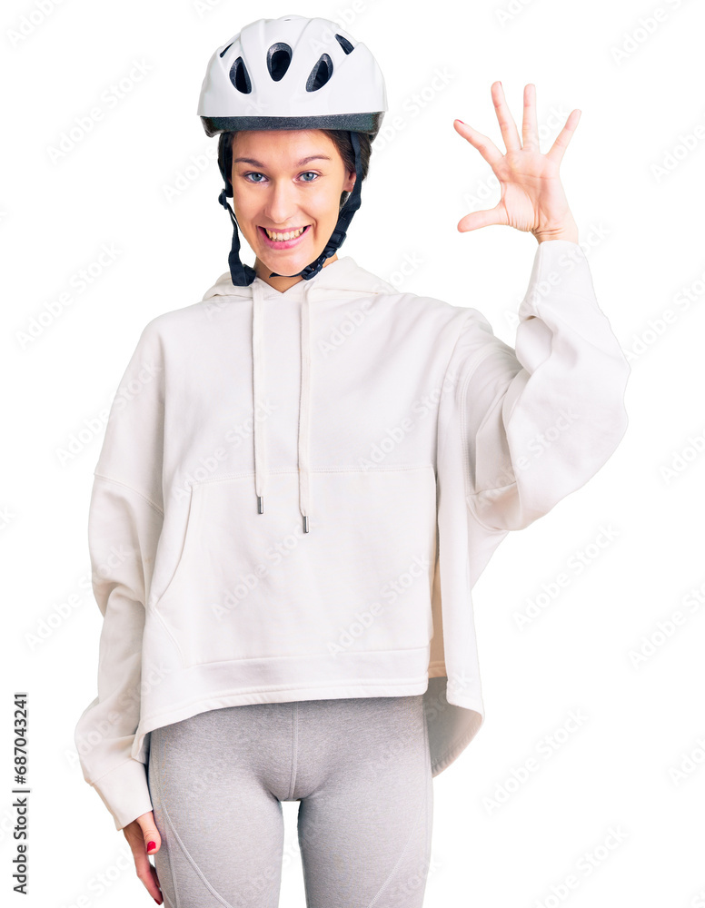 Beautiful brunette young woman wearing bike helmet and sporty clothes smiling and confident gesturing with hand doing small size sign with fingers looking and the camera. measure concept. Beautiful brunette young woman wearing bike helmet and sporty clothes smiling and confident gesturing with hand doing small size sign with fingers looking and the camera. measure concept.