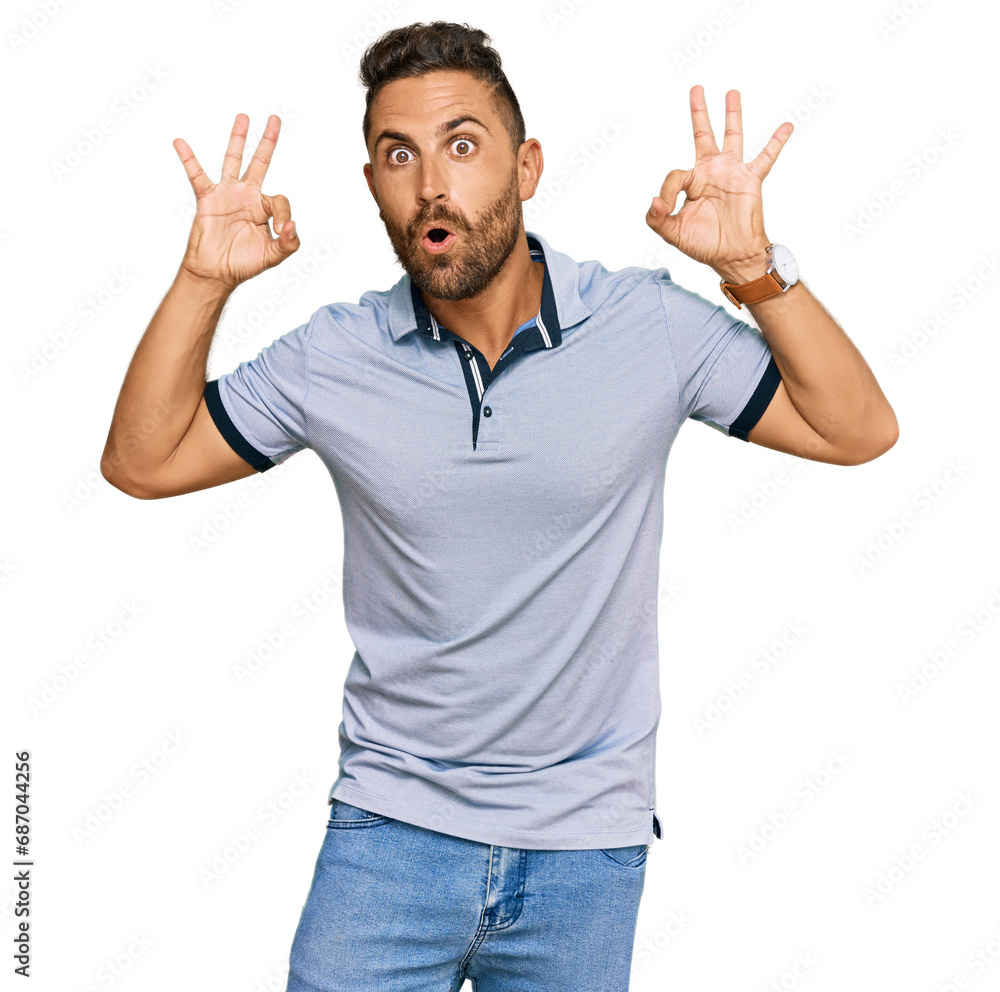 Handsome man with beard wearing casual clothes looking surprised and shocked doing ok approval symbol with fingers. crazy expression Handsome man with beard wearing casual clothes looking surprised and shocked doing ok approval symbol with fingers. crazy expression