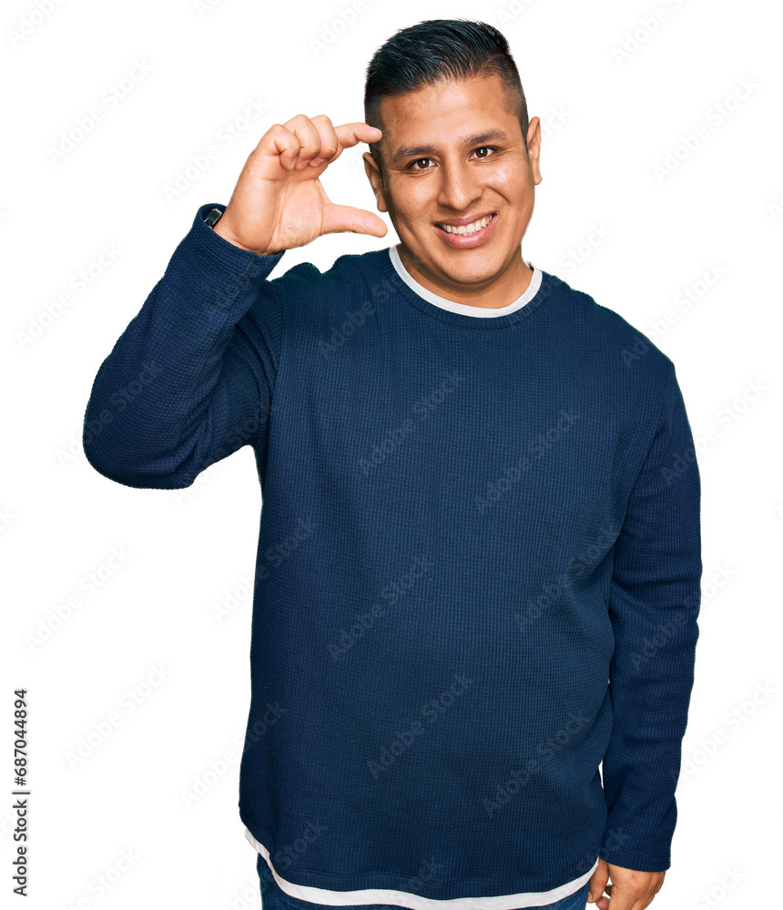 Young latin man wearing casual clothes smiling and confident gesturing with hand doing small size sign with fingers looking and the camera. measure concept. Young latin man wearing casual clothes smiling and confident gesturing with hand doing small size sign with fingers looking and the camera. measure concept.