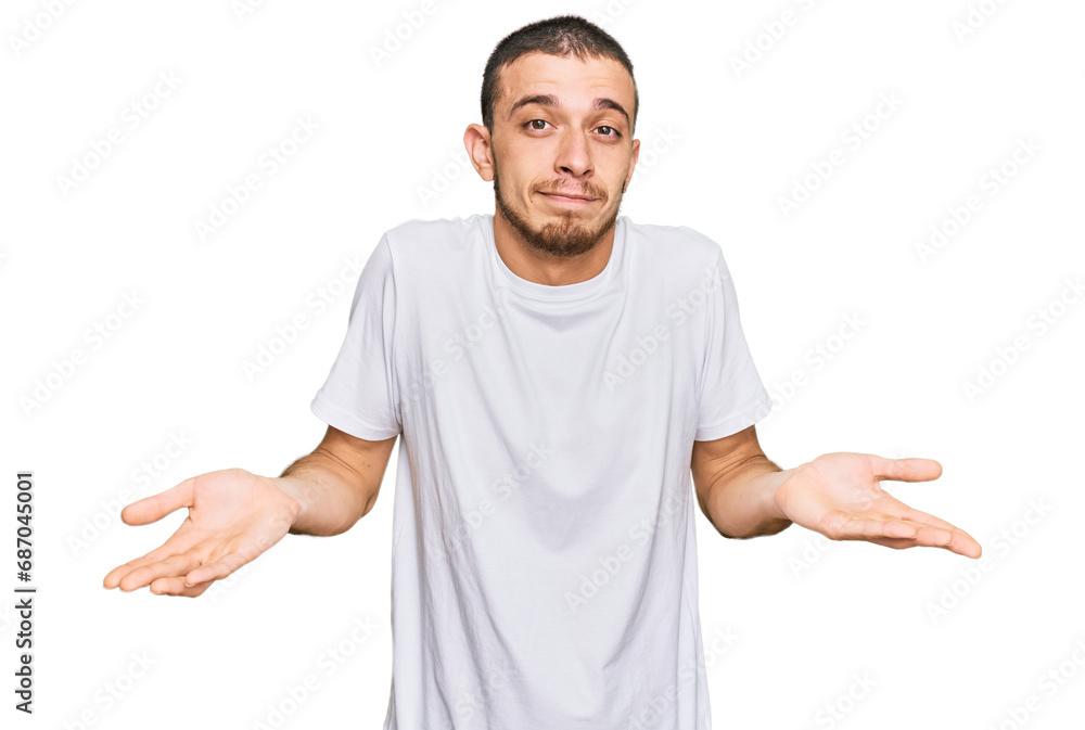 Hispanic young man wearing casual white t shirt clueless and confused expression with arms and hands raised. doubt concept.