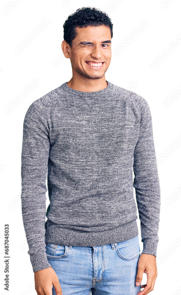 Hispanic handsome young man wearing casual sweater winking looking at the camera with sexy expression, cheerful and happy face.