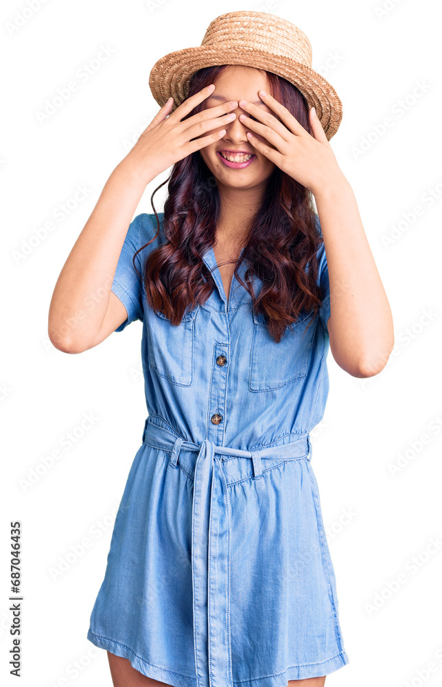 Young beautiful chinese girl wearing summer hat covering eyes with hands smiling cheerful and funny. blind concept. Young beautiful chinese girl wearing summer hat covering eyes with hands smiling cheerful and funny. blind concept.