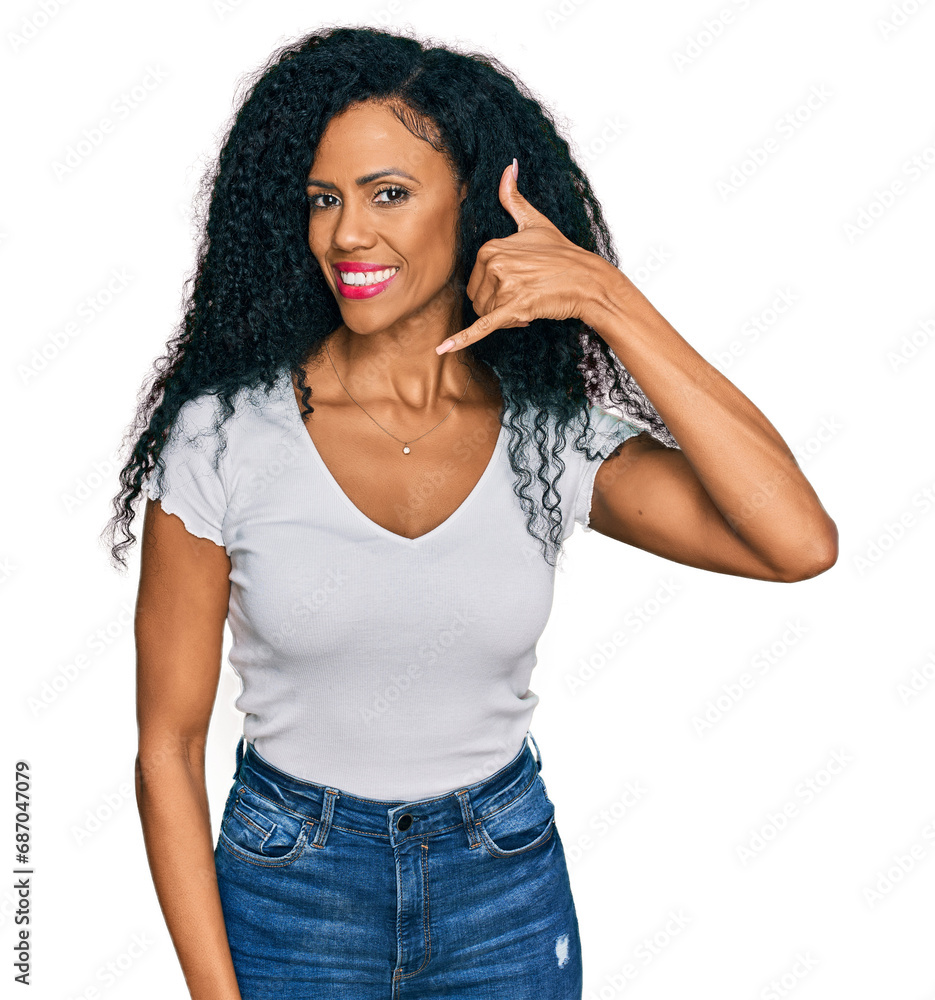 Middle age african american woman wearing casual white t shirt smiling doing phone gesture with hand and fingers like talking on the telephone. communicating concepts. Middle age african american woman wearing casual white t shirt smiling doing phone gesture with hand and fingers like talking on the telephone. communicating concepts.