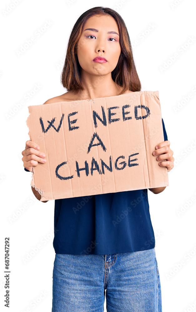 Young beautiful chinese girl holding we need a change banner thinking attitude and sober expression looking self confident Young beautiful chinese girl holding we need a change banner thinking attitude and sober expression looking self confident