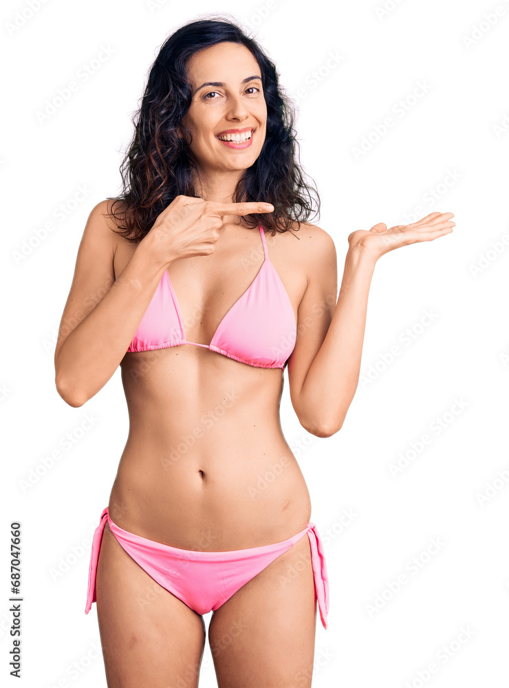 Young beautiful hispanic woman wearing bikini amazed and smiling to the camera while presenting with hand and pointing with finger. Young beautiful hispanic woman wearing bikini amazed and smiling to the camera while presenting with hand and pointing with finger.