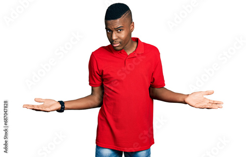 Young african american man wearing casual red t shirt clueless and confused with open arms, no idea concept. photo