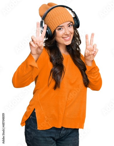 Beautiful brunette young woman listening to music using headphones smiling looking to the camera showing fingers doing victory sign. number two.