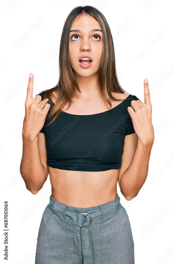Young brunette woman wearing casual clothes amazed and surprised looking up and pointing with fingers and raised arms. Young brunette woman wearing casual clothes amazed and surprised looking up and pointing with fingers and raised arms.