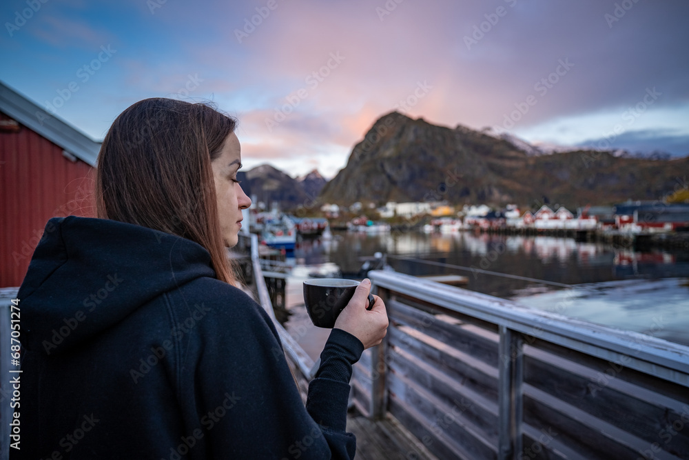 Morning Coffee by the Bay: Woman Enjoying Sørvågen Fisherman Village with Red Houses, Lofoten Islands, Norway