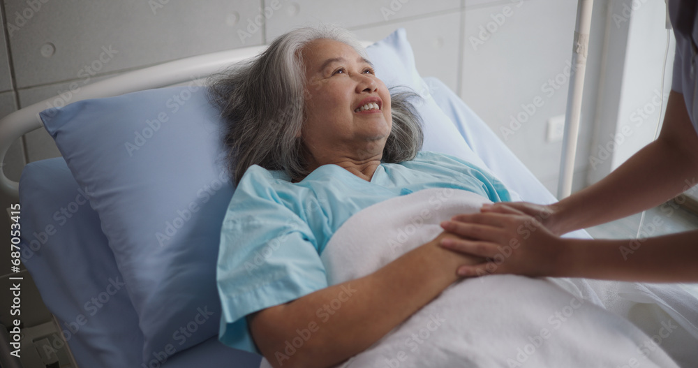 Fototapeta premium Portrait of Young nurse comforting a senior female patient lying in hospital bed,Caregiver and Lifestyle concept