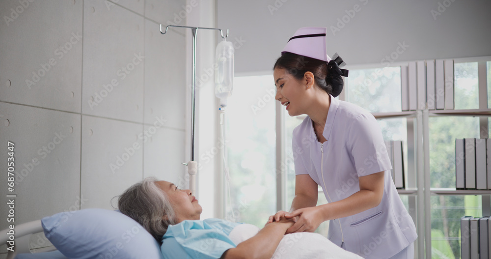Obraz premium Portrait of Young nurse comforting a senior female patient lying in hospital bed,Caregiver and Lifestyle concept