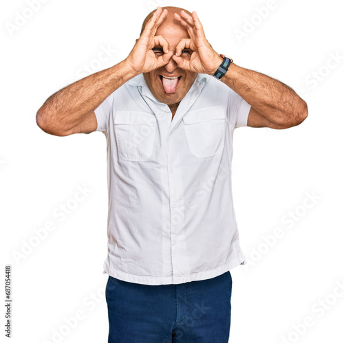 Mature middle east man with mustache wearing casual white shirt doing ok gesture like binoculars sticking tongue out, eyes looking through fingers. crazy expression.