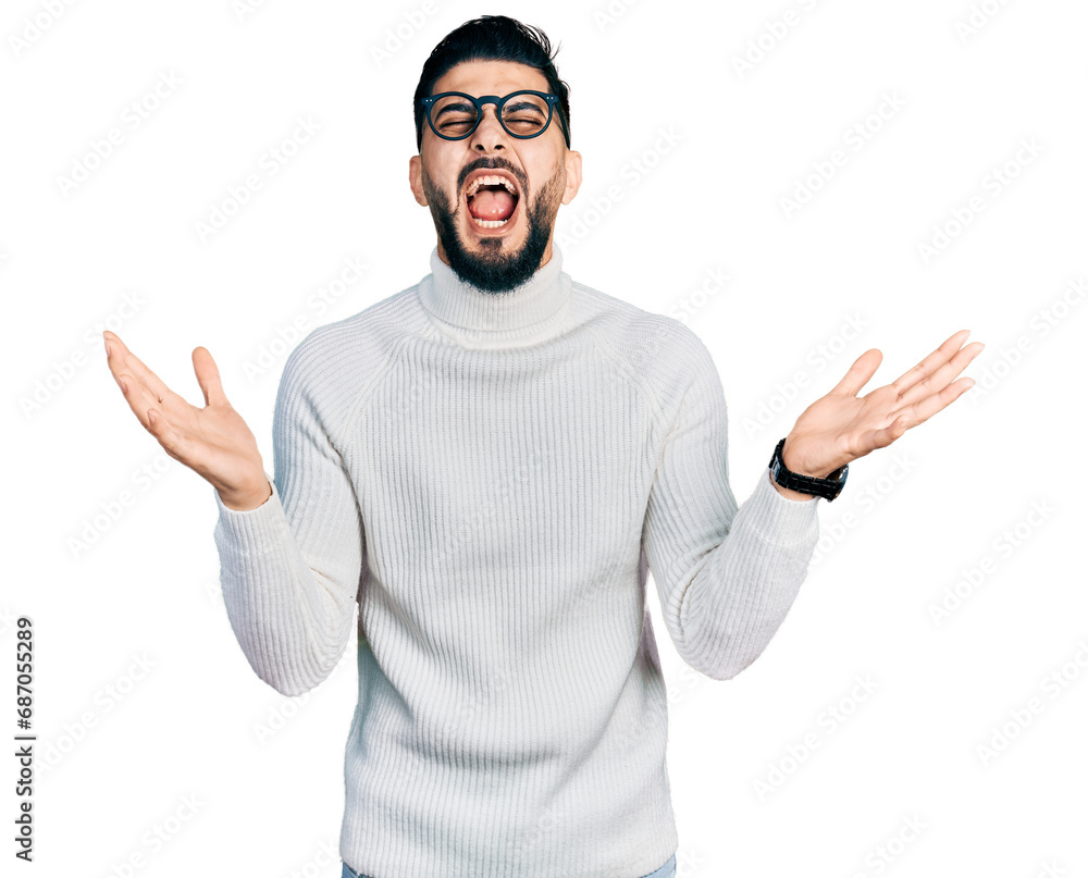Fototapeta premium Young arab man with beard wearing elegant turtleneck sweater and glasses celebrating mad and crazy for success with arms raised and closed eyes screaming excited. winner concept