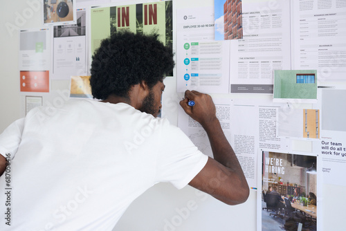 Creative designer standing in front of a moodboard of pending business projects writing notes to improve designs. photo