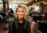 A radiant young woman smiling brightly inside a hair salon, exuding confidence and style in her trendy leather jacket.