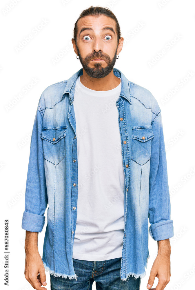 Attractive man with long hair and beard wearing casual denim jacket puffing cheeks with funny face. mouth inflated with air, crazy expression. Attractive man with long hair and beard wearing casual denim jacket puffing cheeks with funny face. mouth inflated with air, crazy expression.