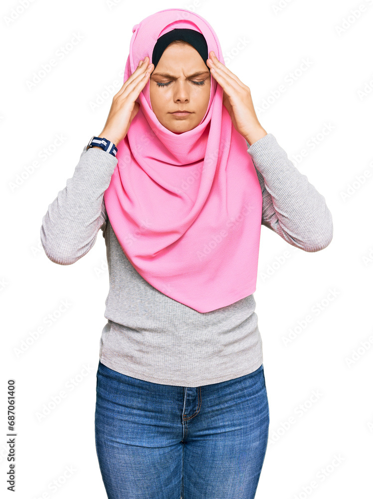 Young caucasian woman wearing traditional islamic hijab scarf suffering from headache desperate and stressed because pain and migraine. hands on head. Young caucasian woman wearing traditional islamic hijab scarf suffering from headache desperate and stressed because pain and migraine. hands on head.