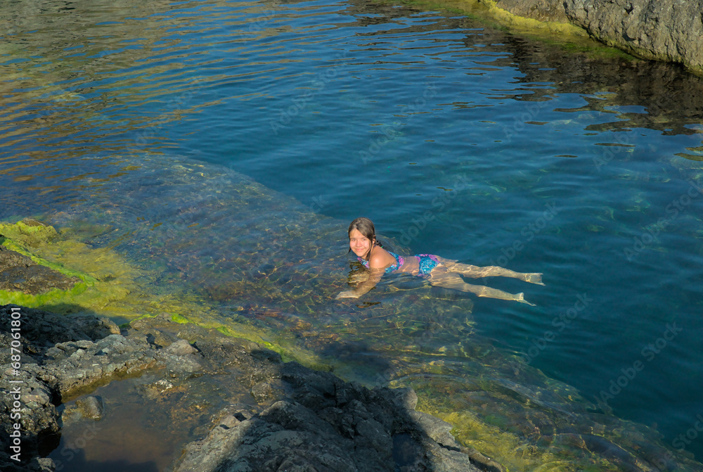 A child swims in the Black Sea among rocks in crystal clear water. Summer holiday at sea, health and entertainment