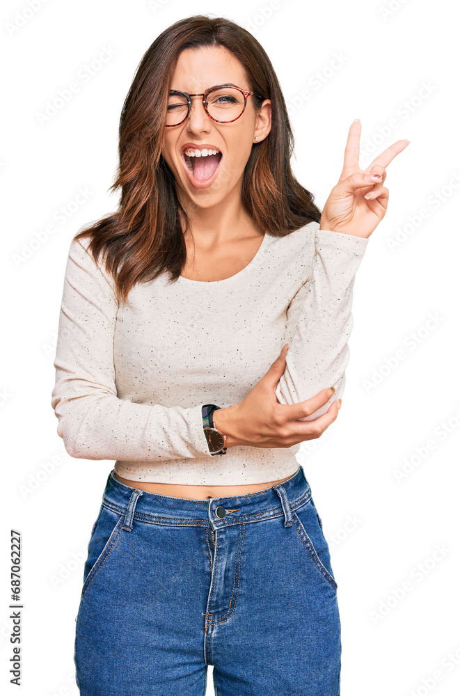 Φωτογραφία Young brunette woman wearing casual clothes and glasses smiling with happy face winking at the camera doing victory sign