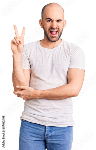 Young handsome man wearing casual t shirt smiling with happy face winking at the camera doing victory sign. number two.