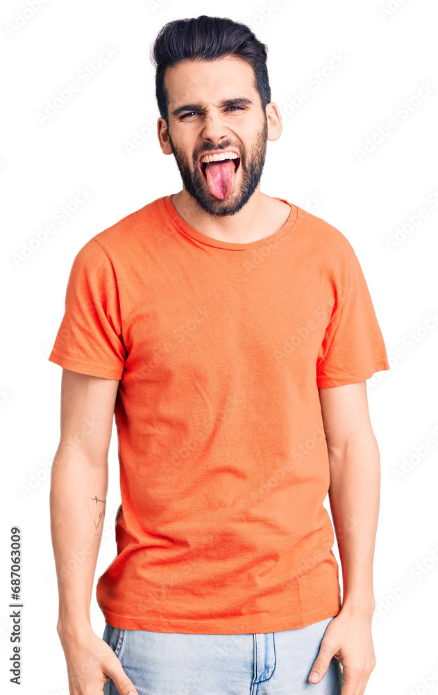 Obraz premium Young handsome man with beard wearing casual t-shirt sticking tongue out happy with funny expression. emotion concept.